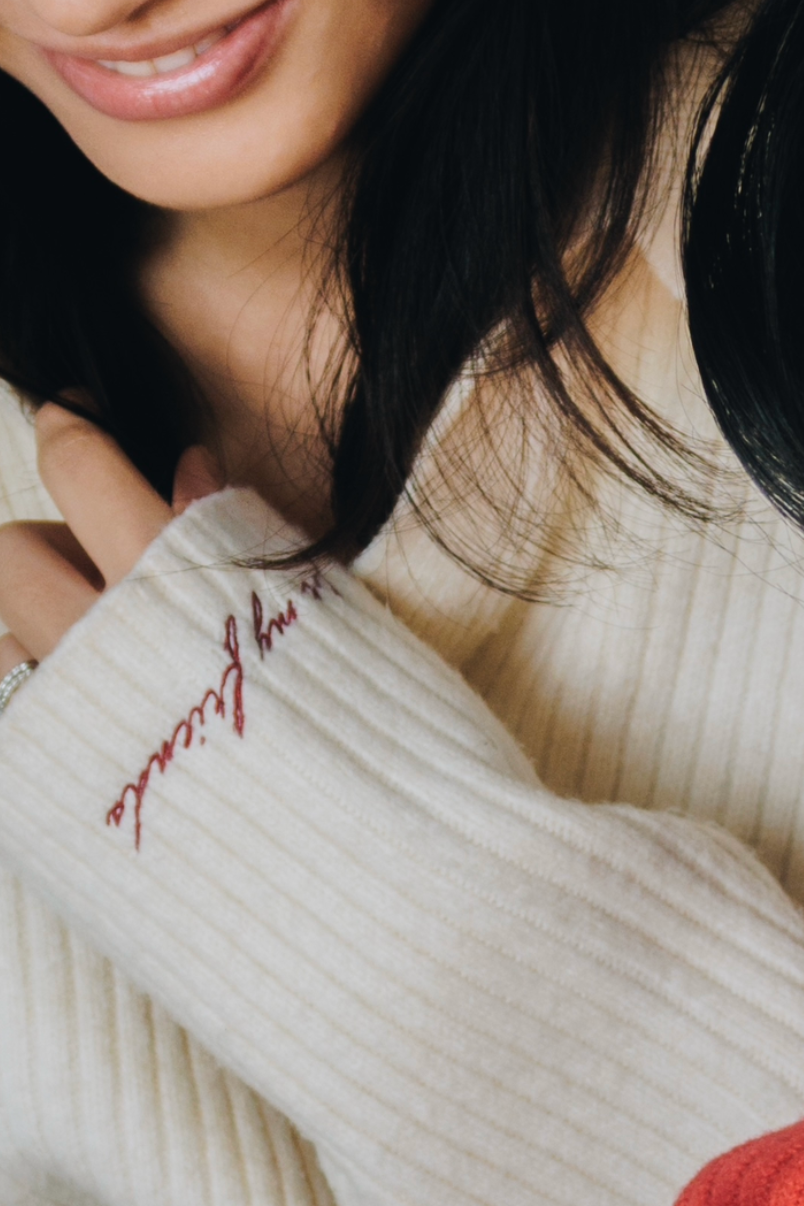 Close-up of a person wearing a cream-colored sweater with red text on the sleeve.