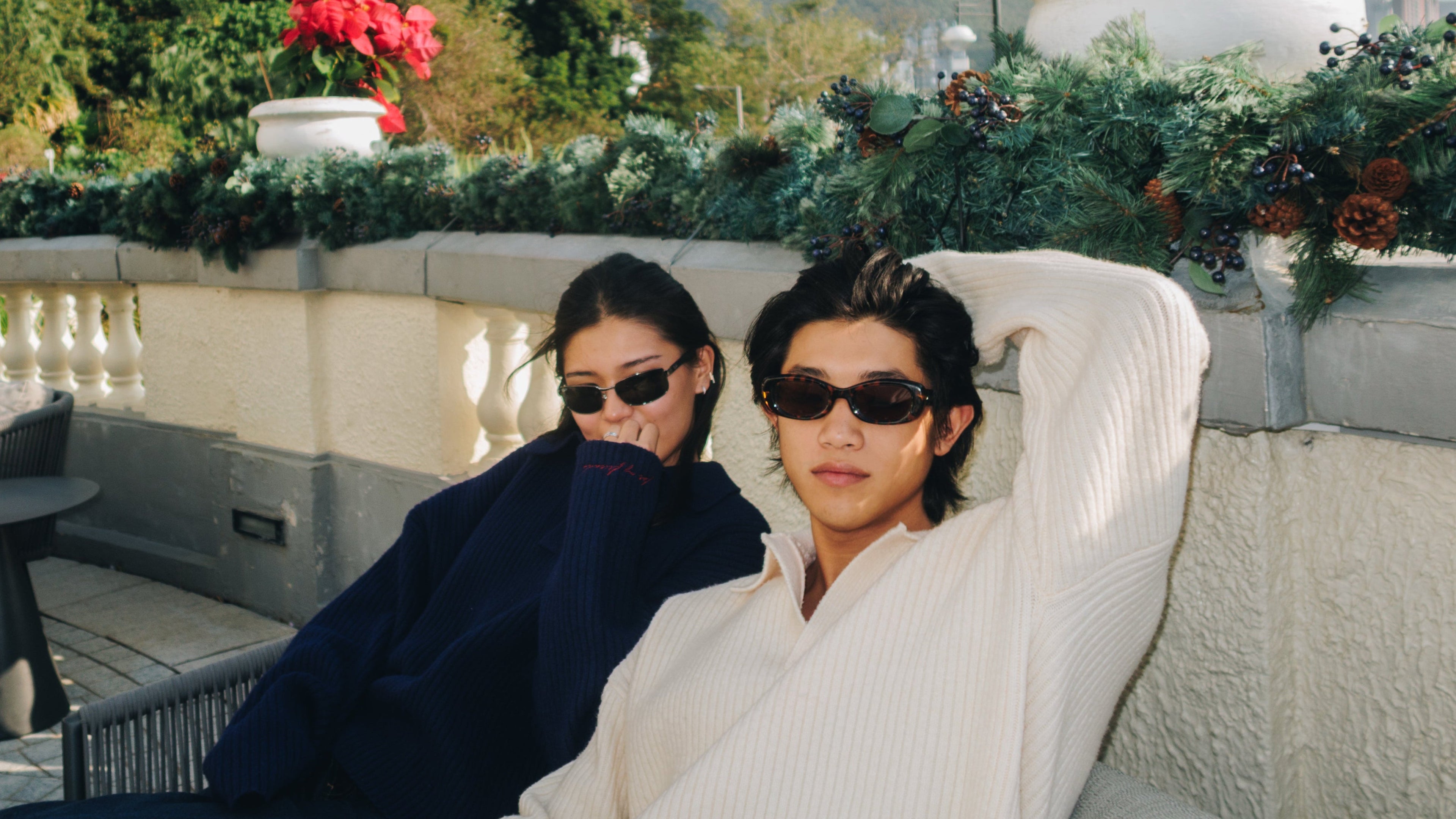 Two people sitting on a rooftop with decorative plants and mountains in the background